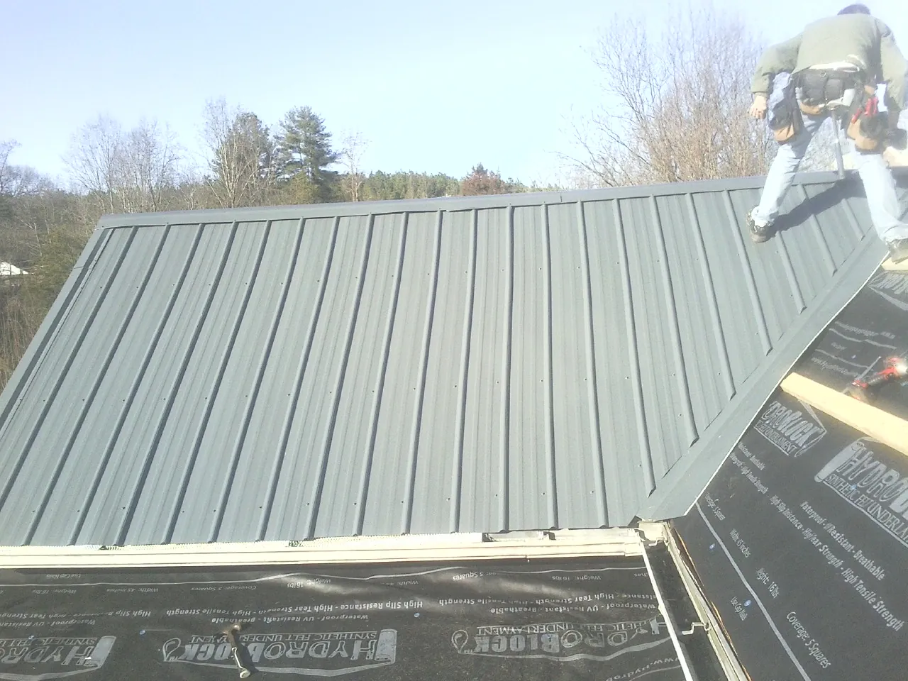 Crew installing dark green standing seam panels over synthetic underlayment in Williamstown